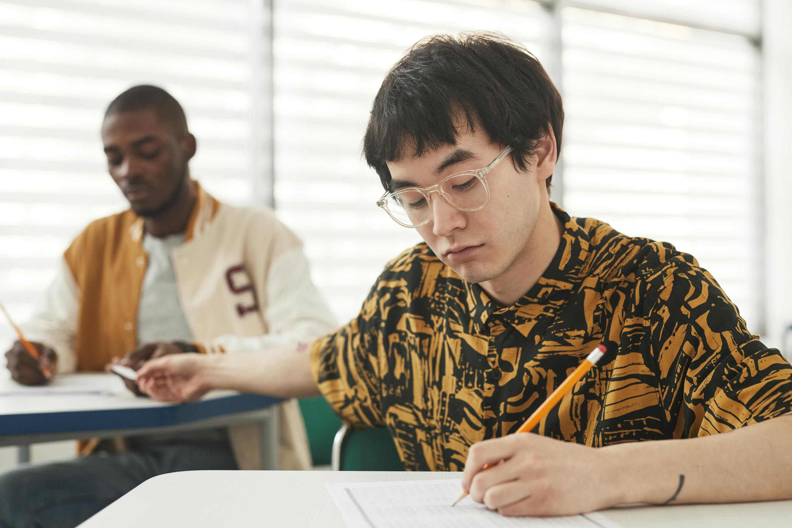 Students sitting at desks in a classroom taking an exam, focusing on their papers.