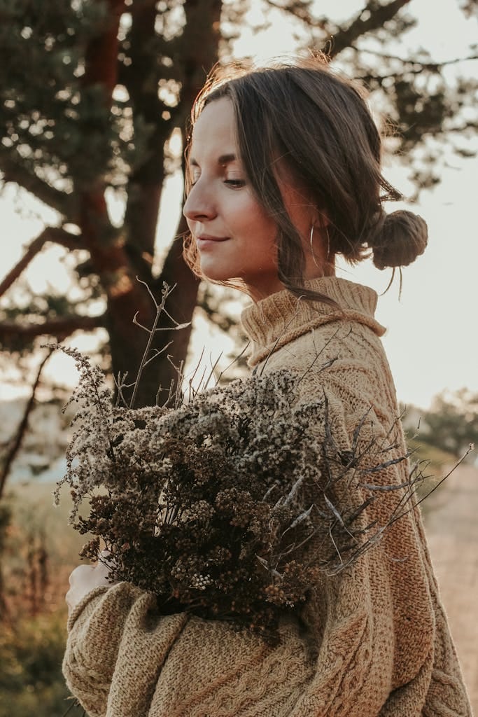 Stylish woman in brown knitted sweater holding dried flowers outdoors.